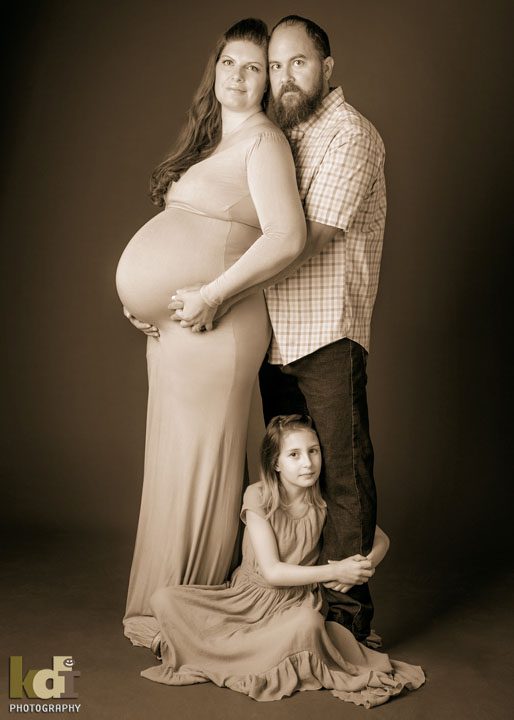Studio maternity portrait - pregnant couple snuggles with daughter