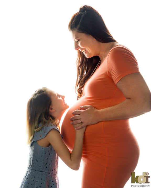 Studio maternity portrait - pregnant mother laughs with her daughter