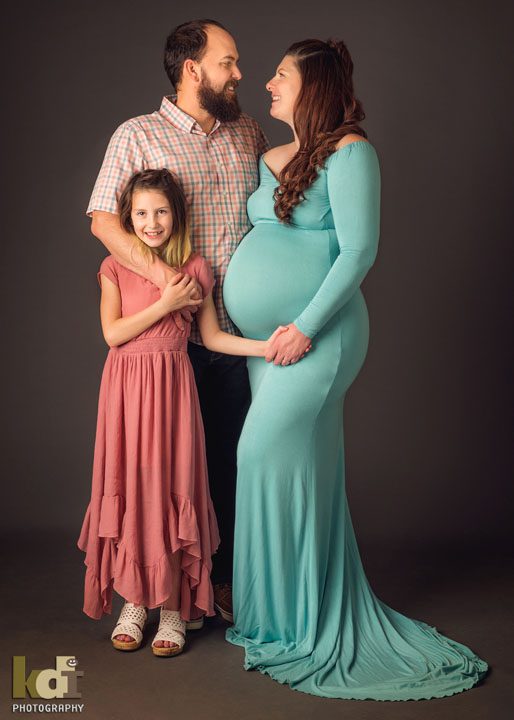 Studio maternity portrait - pregnant couple laughs with daughter