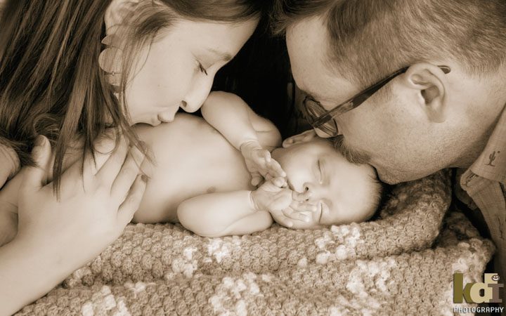 Black and white studio portrait of parents kissing their sleeping newborn baby, newborn photography in Flagstaff, AZ