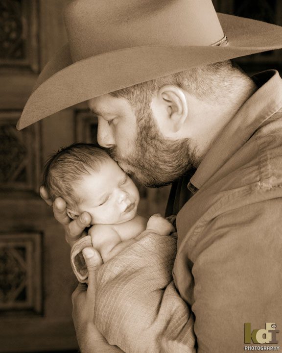 father in cowboy hat kisses his newborn son, baby boy in Flagstaff, AZ