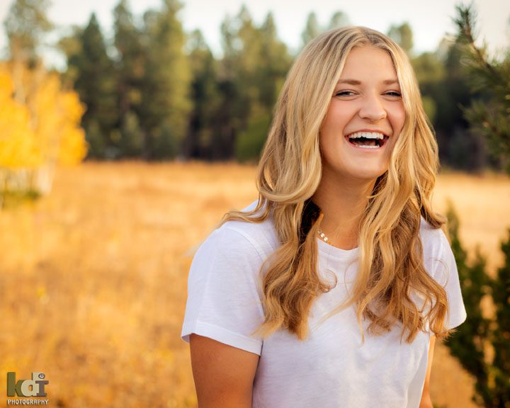 senior portrait of girl laughing with colorful fall trees in background,  Flagstaff, AZ