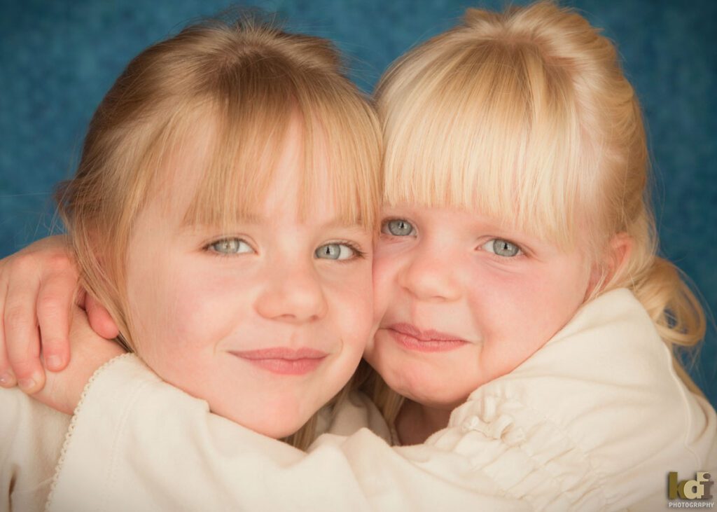Color studio portrait of sisters snuggling cheek to cheek, by Flagstaff photographer.
