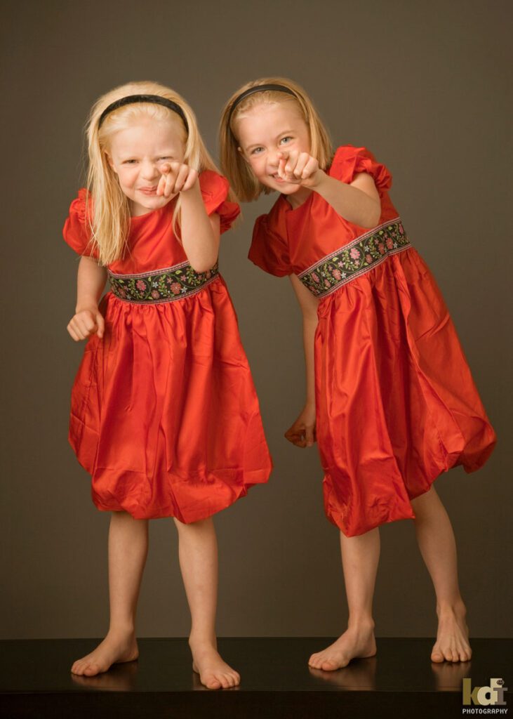 Color studio portrait of sisters standing and pointing at camera, in Flagstaff photography studio.