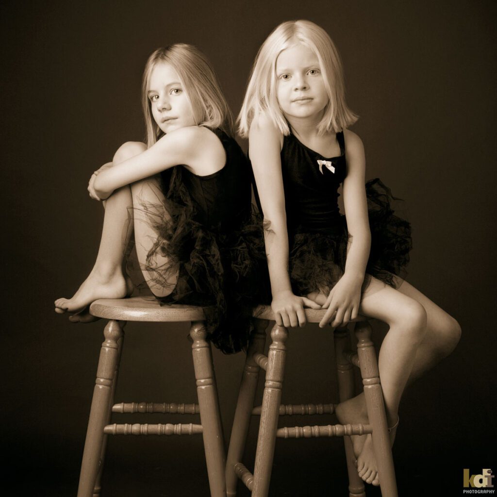 Black and white studio portrait of sisters sitting on stools in tutus, in Flagstaff photography studio.