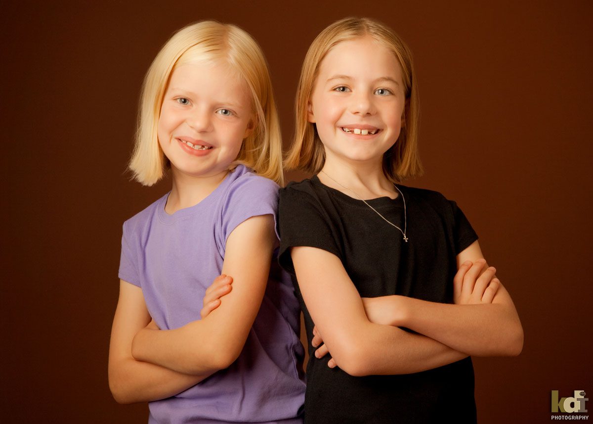 Color studio portrait of young sisters sitting with arms crossed, in Flagstaff photography studio.