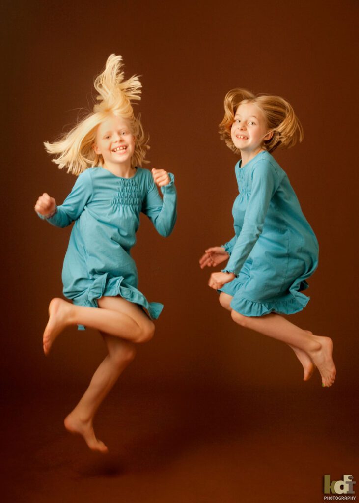 Color studio portrait of sisters jumping in blue dresses in Flagstaff photography studio.
