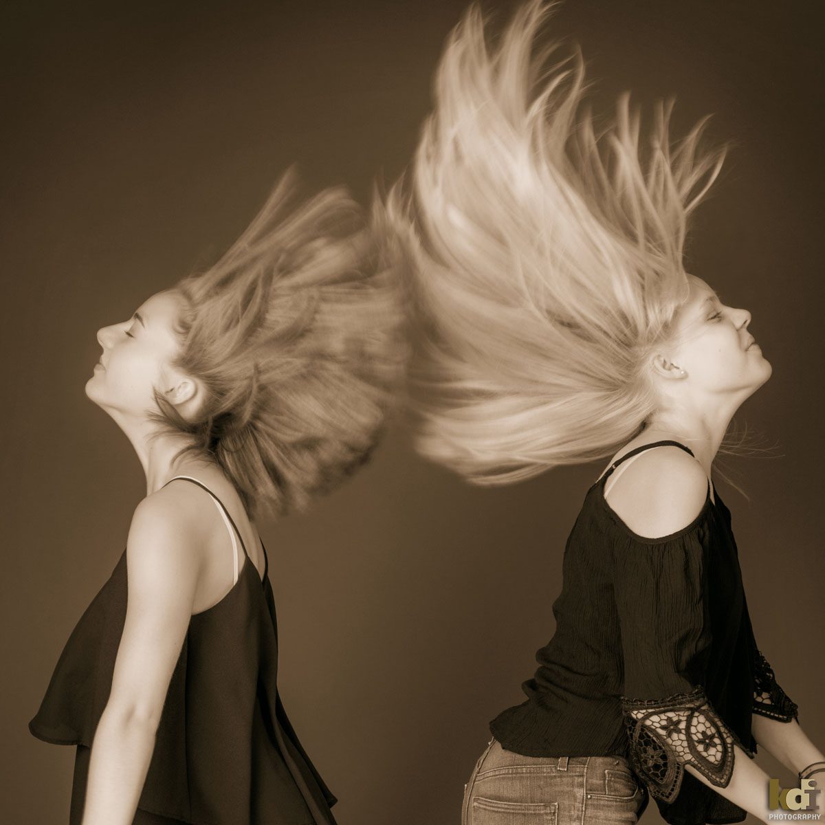 Black and white studio portrait of sisters flipping their hair.