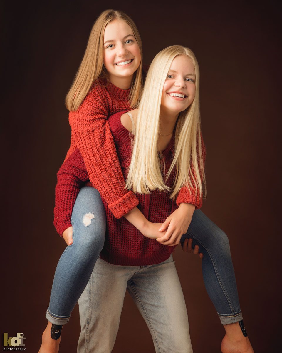 Color studio portrait of sisters on piggyback in Flagstaff photography studio.