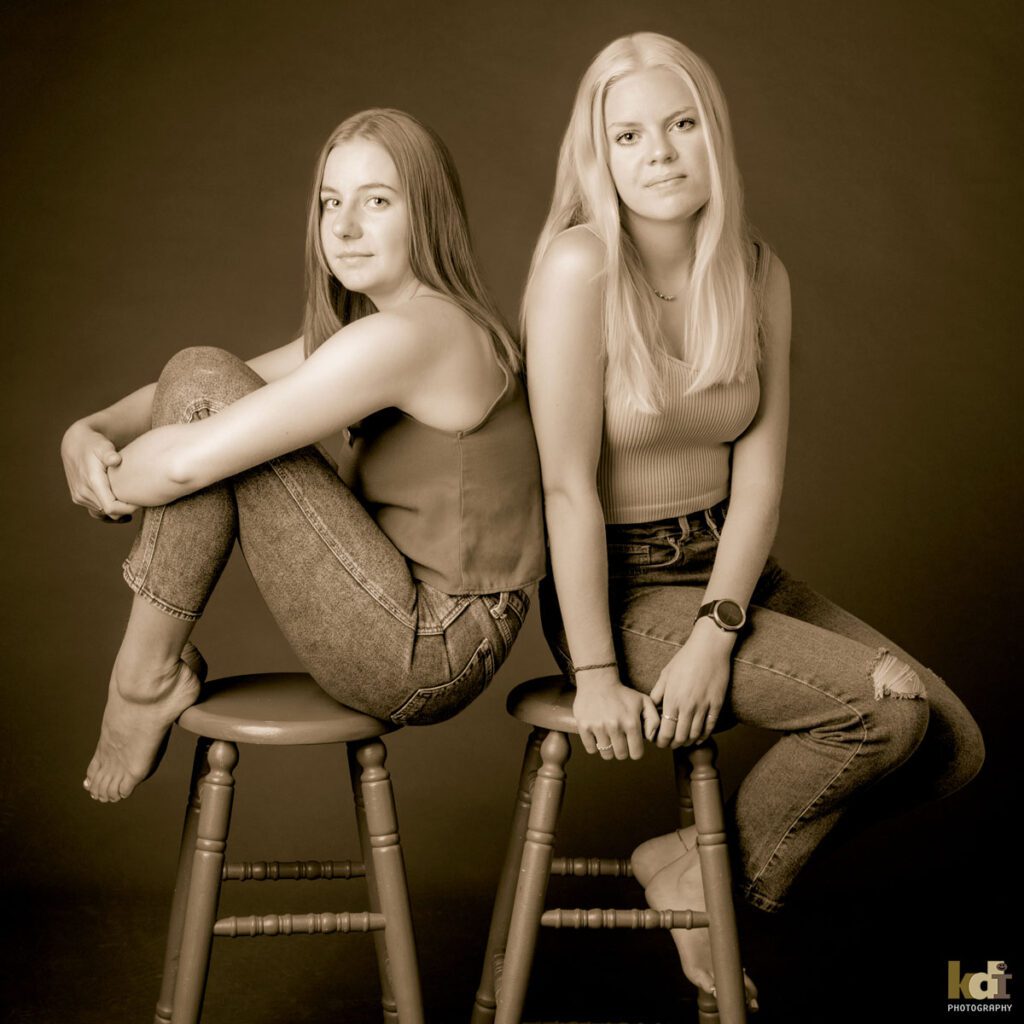 Black and white studio portrait of teenage sisters sitting on stools, in Flagstaff photography studio.