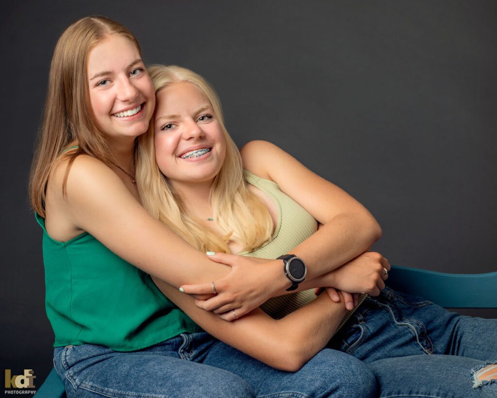 Color studio portrait of teenage sisters sitting snuggled on bench, in Flagstaff photography studio.