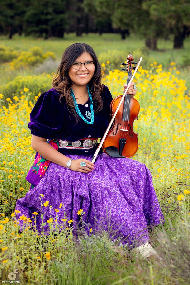 Senior portrait of girl sitting in yellow  flowers, wearing Navajo traditional dress, holding her violin, near the San Francisco Peaks, in Northern Arizona, Flagstaff AZ, Coconino County. ©KDI Photography