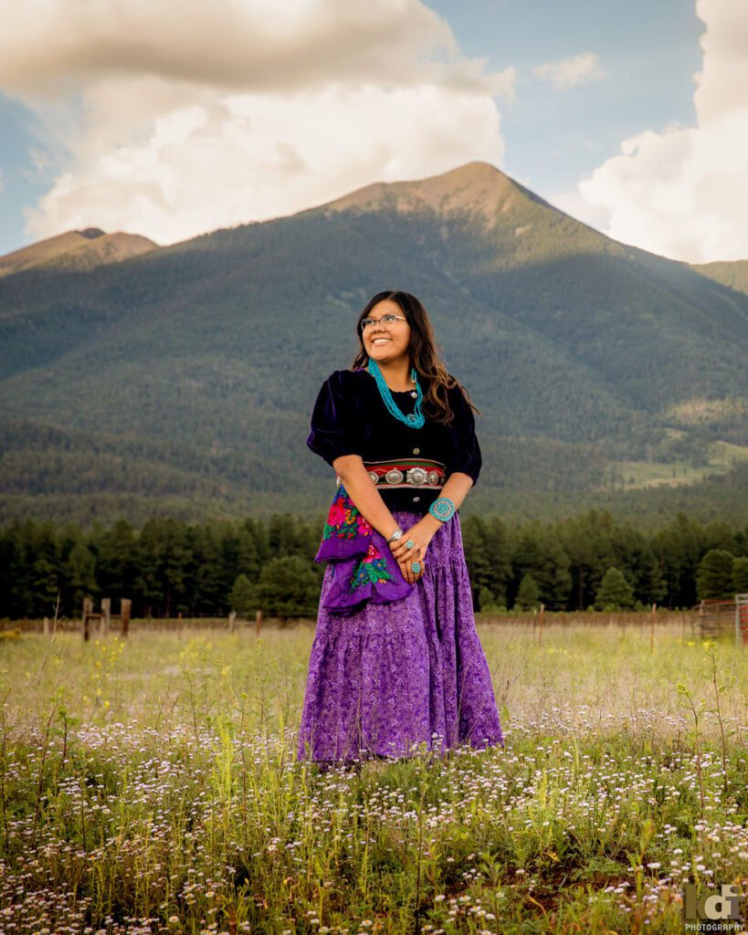 Senior portrait of girl in Navajo traditional dress in front of the San Francisco Peaks, in Northern Arizona, Coconino County, Flagstaff AZ. ©KDI Photography