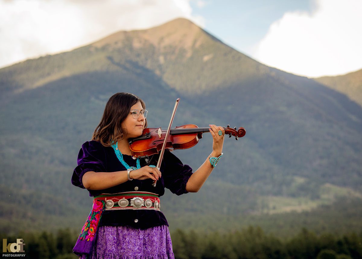 Senior portrait of girl in Navajo traditional dress, playing violin in front of the San Francisco Peaks, in Northern Arizona, Coconino County, Flagstaff AZ. ©KDI Photography