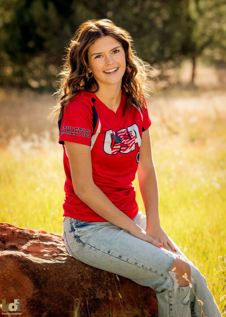 Softball player sits on rock wearing team colors, Flagstaff senior photos, by KDI Photography.