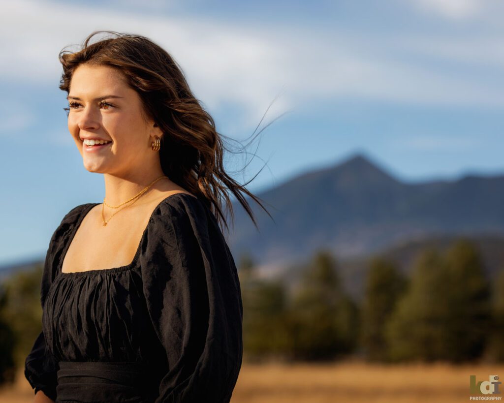 Coconino High School athlete wearing a black dress, smiling at sunset, with the San Francisco Peaks behind her, Flagstaff senior photos, by KDI Photography.