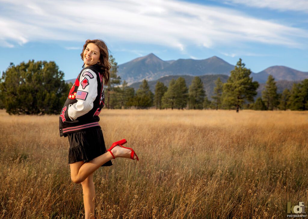 Coconino High School athlete wearing her letterman jacket, kicks up her red high heel shoes, Flagstaff senior photos, by KDI Photography.