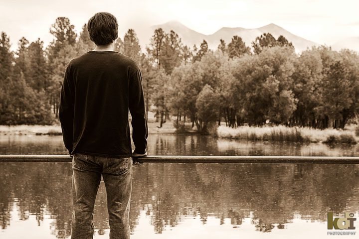 High school senior boy looks out over water in Flagstaff, San Francisco Peaks. Senior photos by KDI Photography.