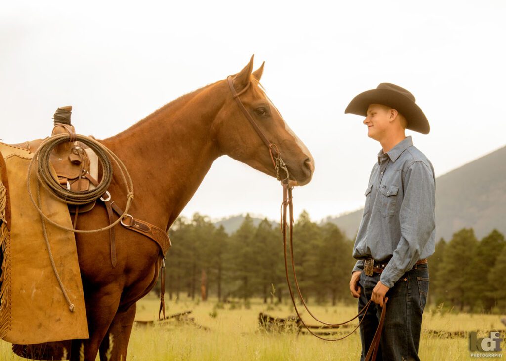 Senior photo of cowboy looking at his horse in the mountains of Flagstaff, AZ, KDI Photography