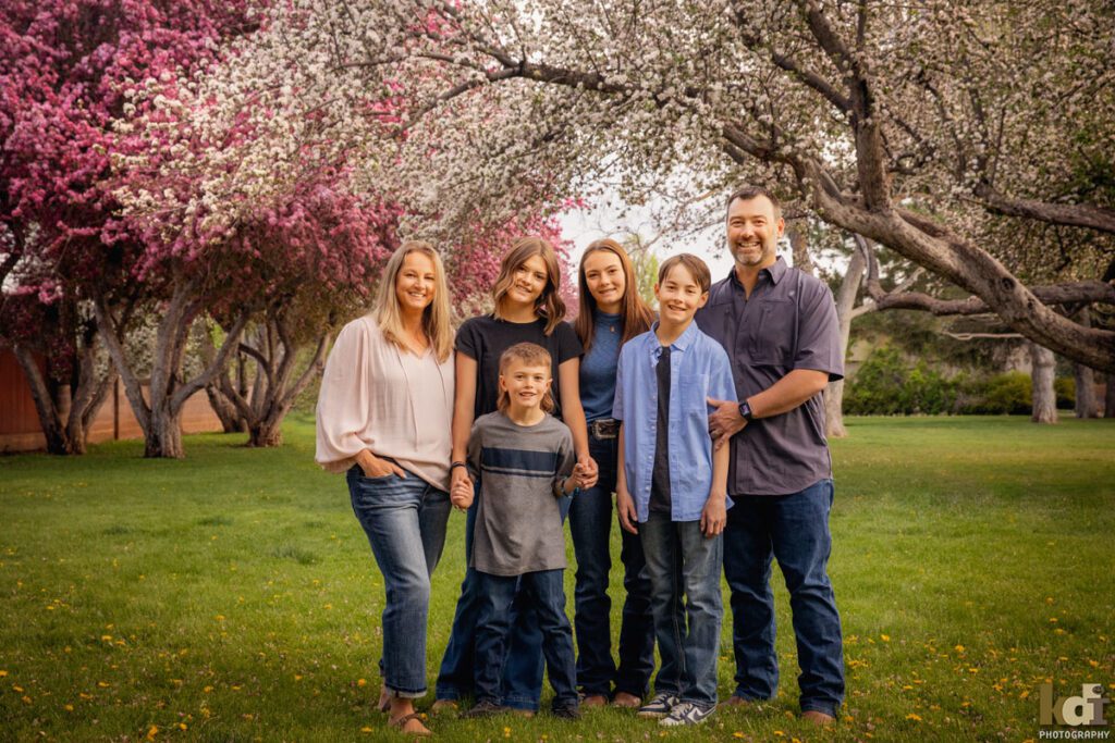 Family portrait of family of six, smiling, snuggled together, under flowering trees, Downtown Flagstaff, AZ Portraits by KDI Photography