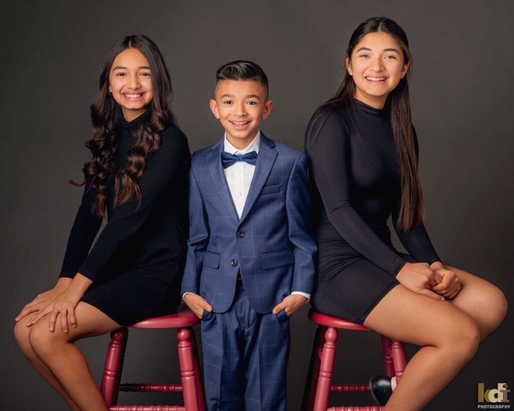 Studio Portrait of Three Siblings, Two Older Sisters Sit On Either Side of  their Younger Brother in Family Portrait in Flagstaff, AZ © KDI Photography