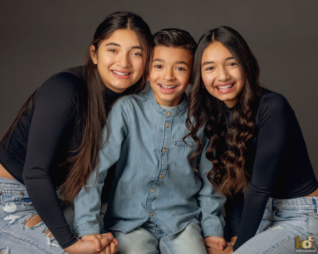 Studio Portrait of Three Siblings, Two Older Sisters Laughing with their Younger Brother in Family Portrait in Flagstaff, AZ © KDI Photography