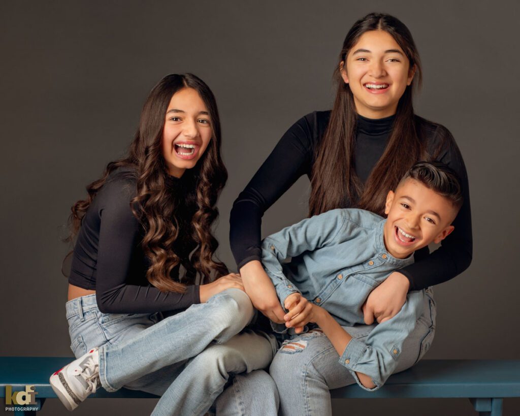 Studio Portrait of Three Siblings, Two Older Sisters Tickling their Younger Brother in Family Portrait in Flagstaff, AZ © KDI Photography
