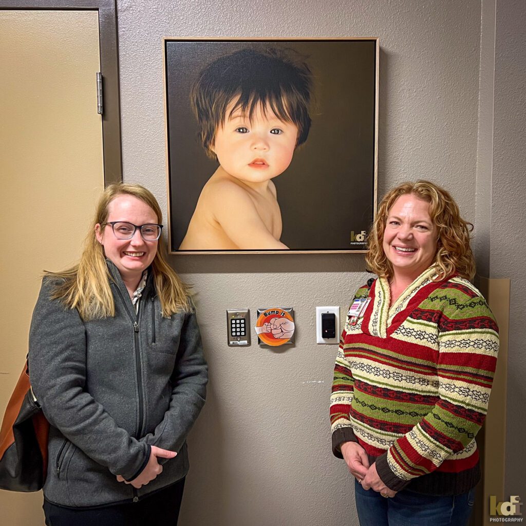 A Mother and the Clinical Manager of the Flagstaff Special Care Nursery, Standing in Front of Wall Art Portrait of Baby, Family Photo Session, Parents with a Newborn, Studio Portraits in Northern Arizona, Family Portraits by KDI Photography