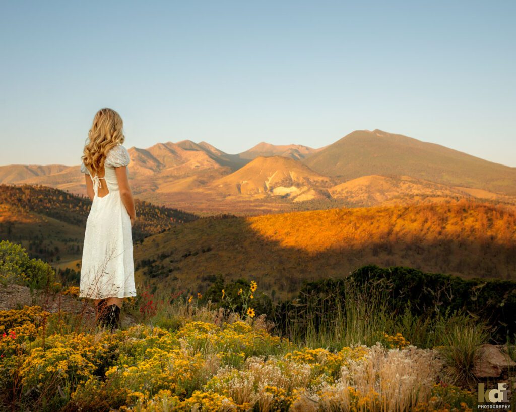 Senior Photos of a Girl in White Dress Standing in a Field of Wildflowers Looking Out at the San Francisco Peaks of Northern Arizona, Location Portraits by KDI Photography