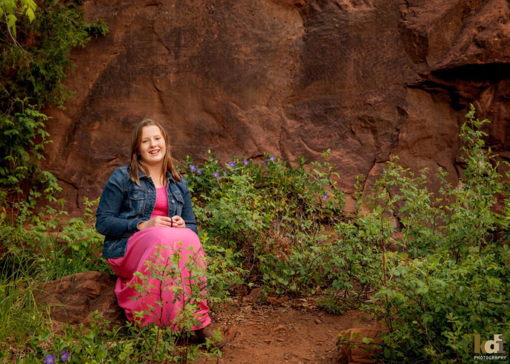 Portrait of tween girl sitting near red rocks, with purple flowers next to her in Sedona AZ, photographic art by KDI Photography. 