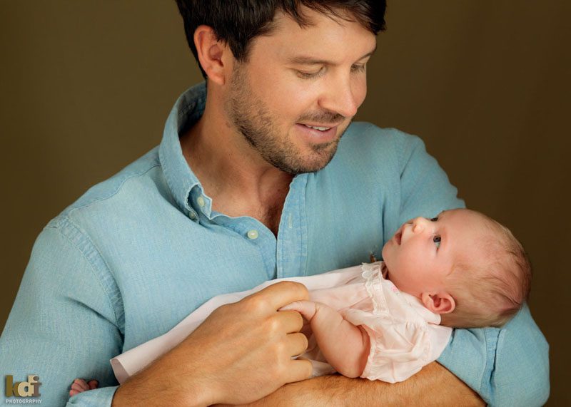 Family photos of a a father snuggling a newborn holding her hand and smiling at her cute expression, studio portraits in Northern Arizona, family portraits by KDI Photography
