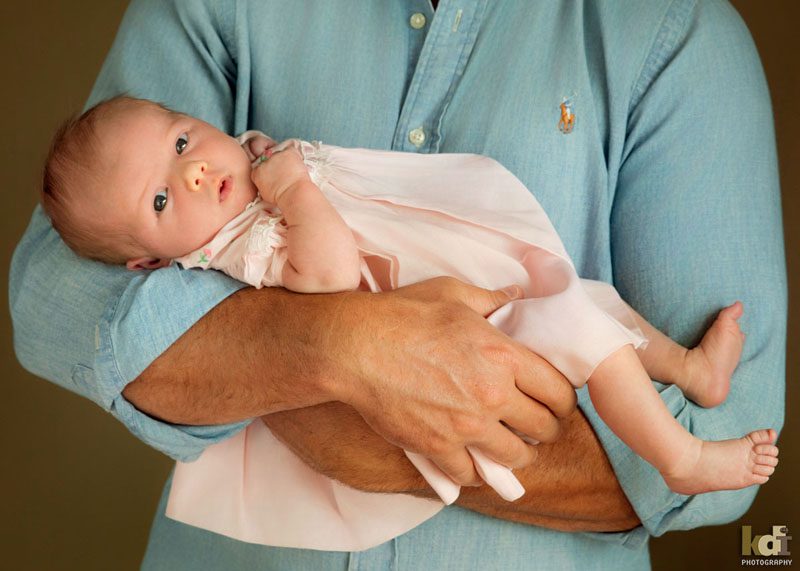 Family photos of a a father snuggling a newborn holding who is looking at the camera with a cute expression, studio portraits in Northern Arizona, family portraits by KDI Photography