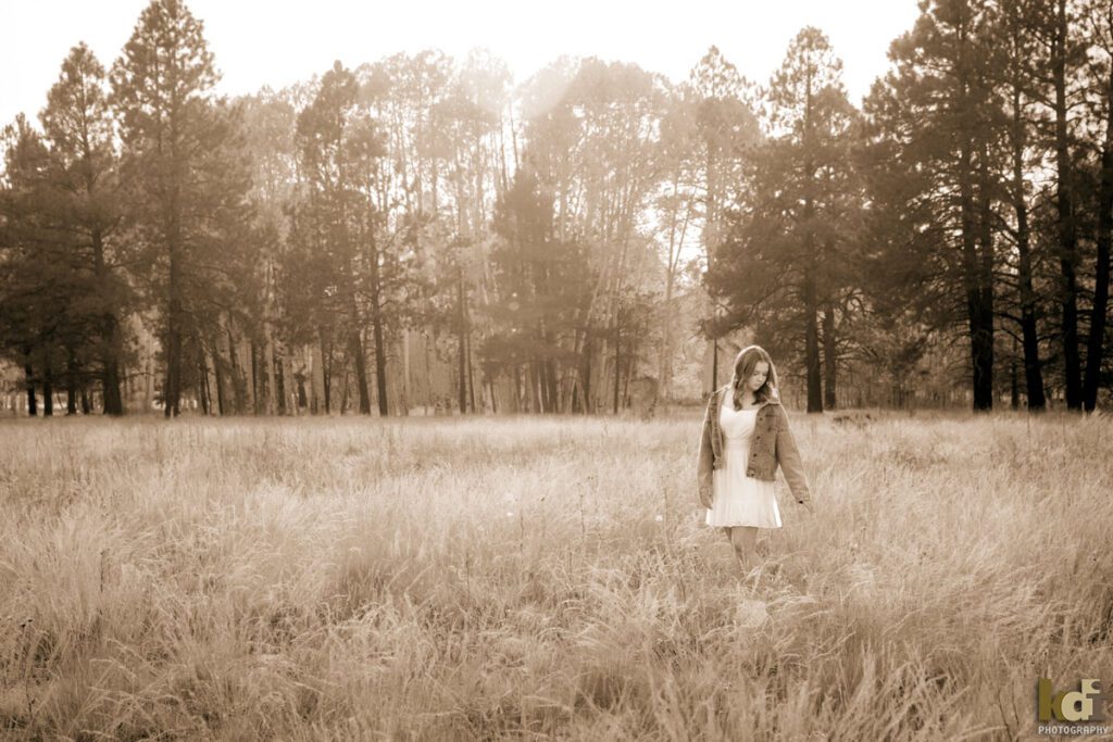 Black and white high school senior photo showing girl with blond hair, in white dress and jean jacket among the fall aspen trees, portrait photography in Flagstaff AZ by senior photographer KDI Photography
