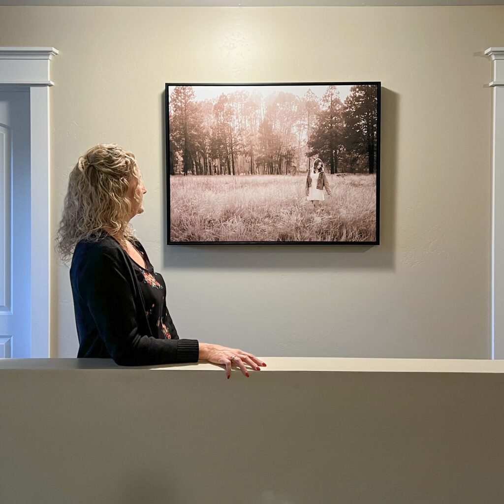 A mother looks at a framed canvas wall art portrait featuring a black and white photograph of her daughter, a high school senior photo showing girl with blond hair, in white dress and jean jacket among the fall aspen trees, portrait photography in Flagstaff AZ by senior photographer KDI Photography