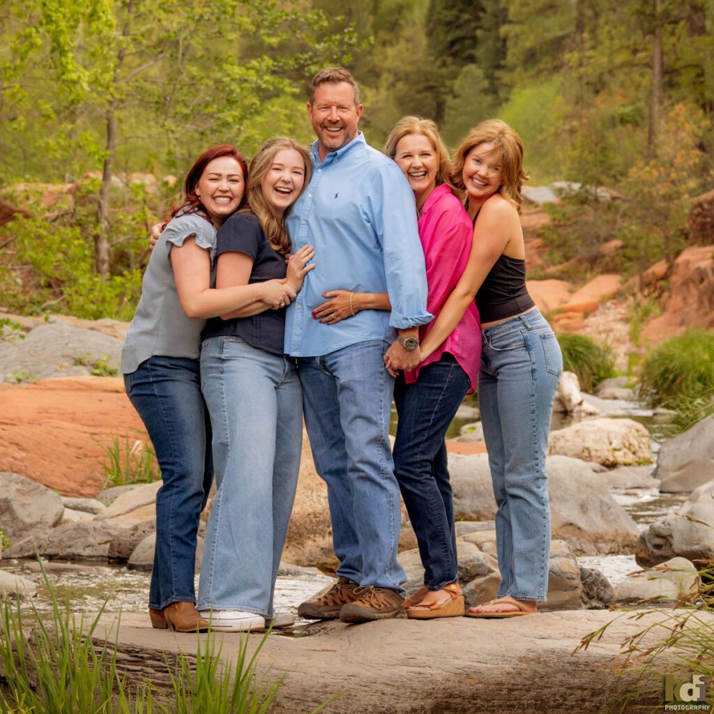 Family photos by Flagstaff photographic artist KDI Photography that features a father and mother, snuggling with their three adult daughters, standing on a rock in Oak Creek, family photos in Sedona, AZ