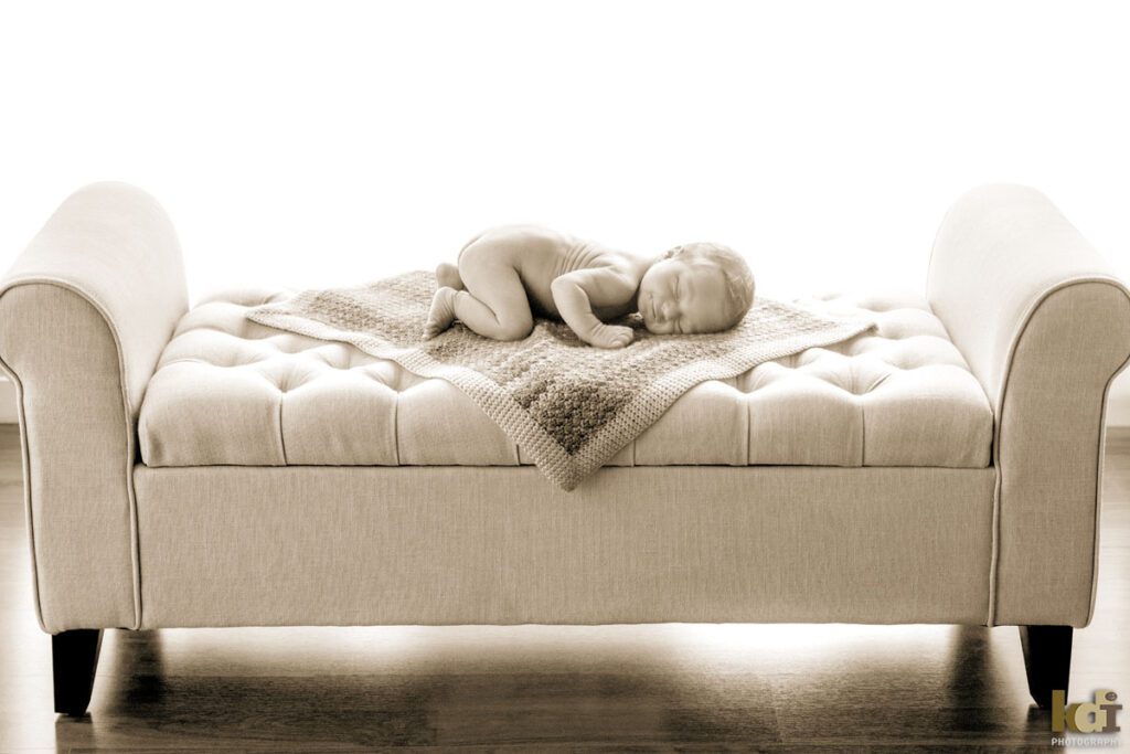 Black and white newborn photography, portrait of a new baby boy, asleep, smiling, lying on blanket on a small couch, in a photo studio in Flagstaff by newborn and family photographer, KDI Photography
