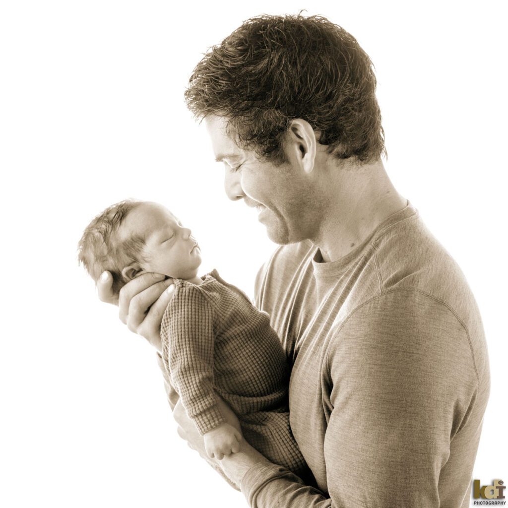 Black and white newborn photography, portrait of a father and new baby boy held in his arms, in a photo studio in Flagstaff by newborn and family photographer, KDI Photography
