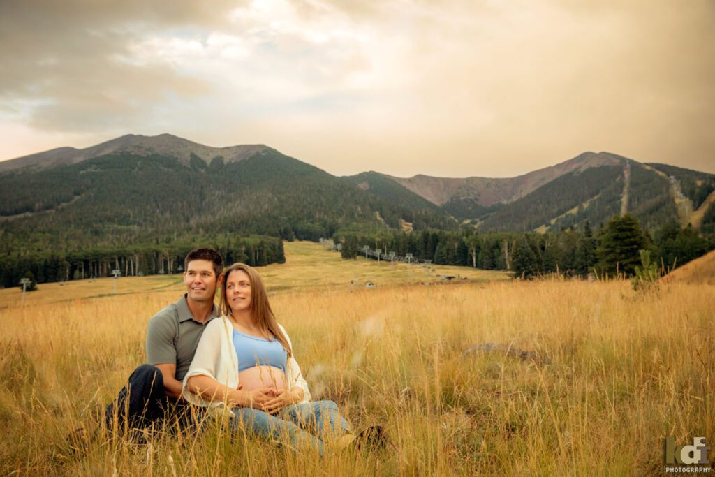 Maternity photo, portrait of a pregnant couple sitting in the grass, on location at the Arizona Snowbowl, in the San Francisco Peaks, by Flagstaff pregnancy photographer, KDI Photography
