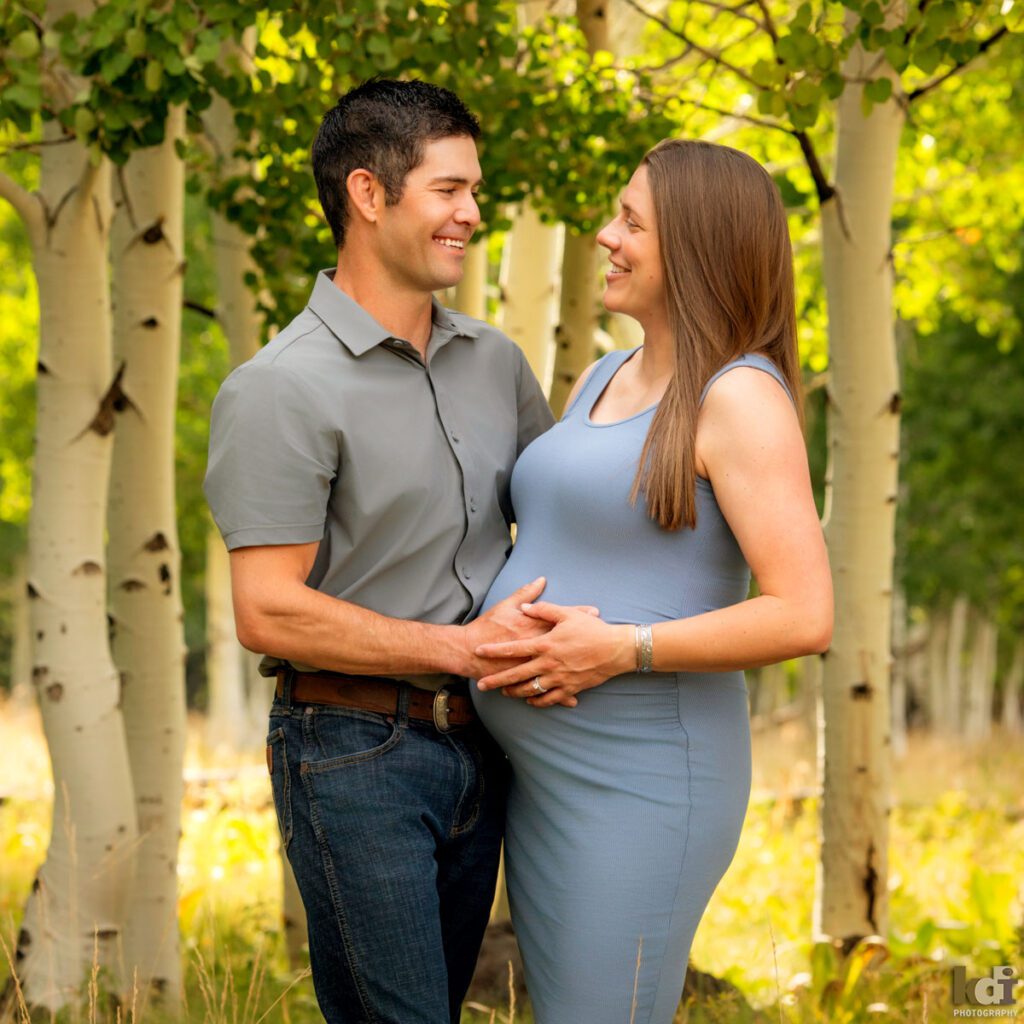 Maternity photography, color portrait of a pregnant couple talking to each other and smiling, on location at the Arizona Snowbowl, in the aspen trees by Flagstaff pregnancy photographer, KDI Photography