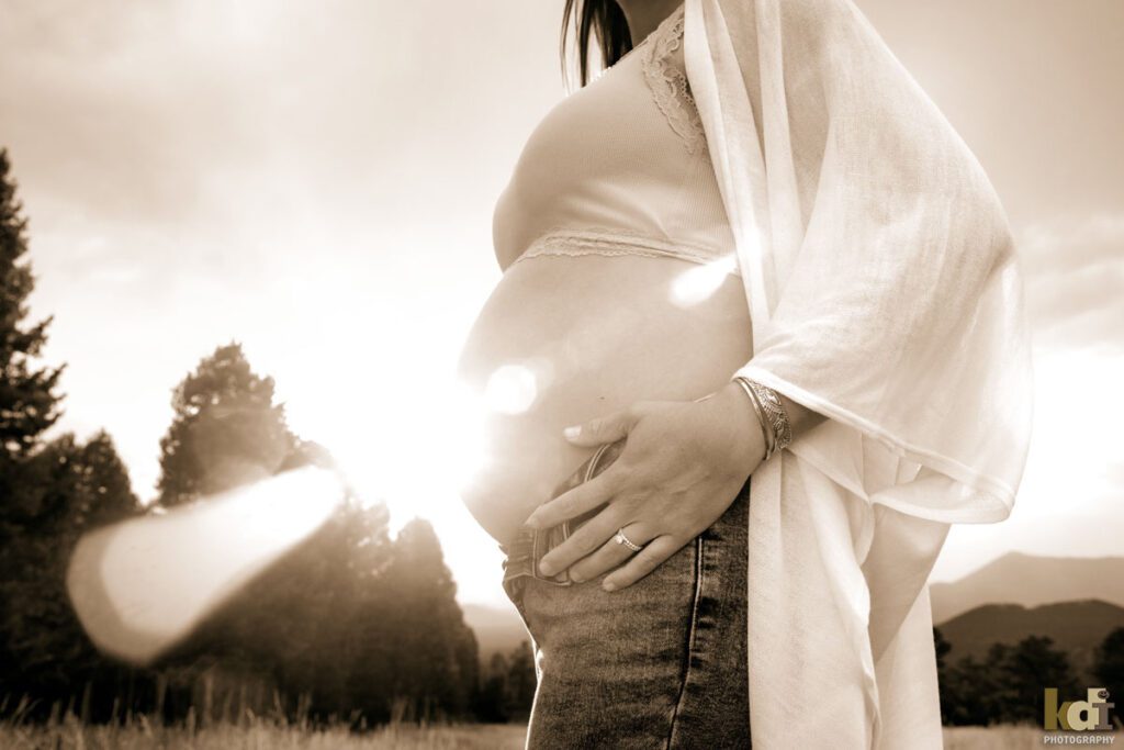 Maternity photo, black and white portrait of a woman's hands on her pregnant belly with sun flare coming across the baby bump, on location at the Arizona Snowbowl, in the San Francisco Peaks, by Flagstaff pregnancy photographer, KDI Photography
