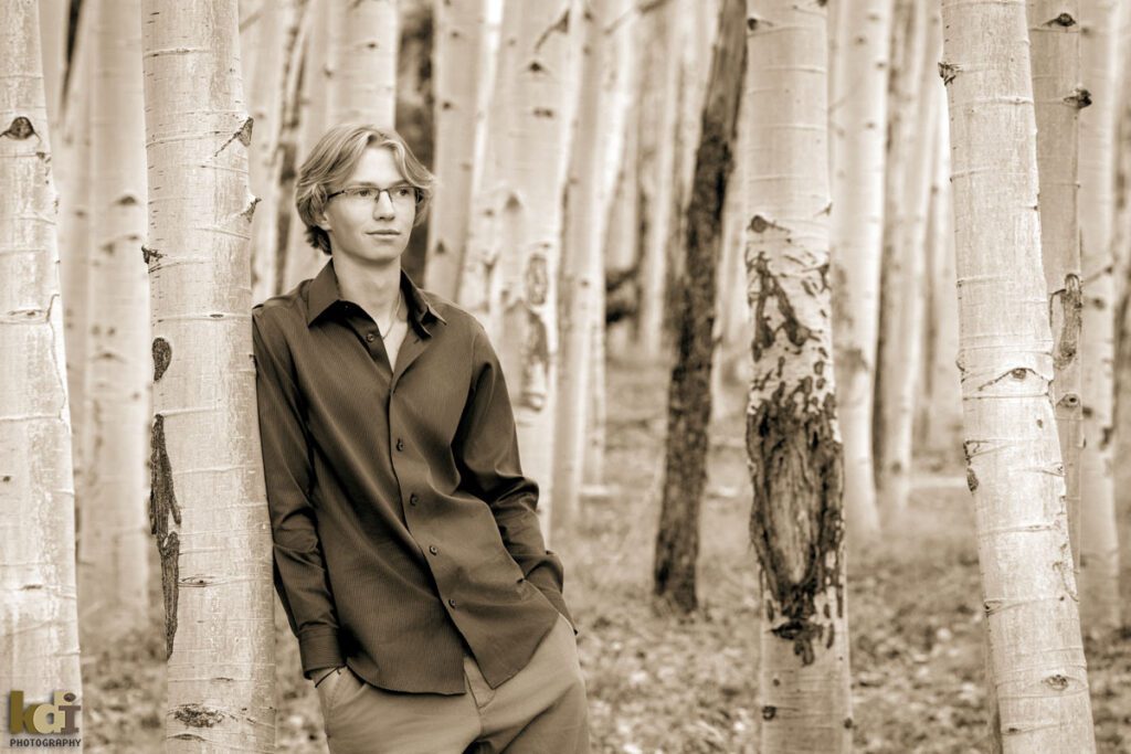 Black and white portrait a rock climber, senior photos of a senior boy looking away, wearing a button down shirt and khaki pants, standing the colorful fall aspens in the mountains of Flagstaff, by family portrait artist, KDI Photography