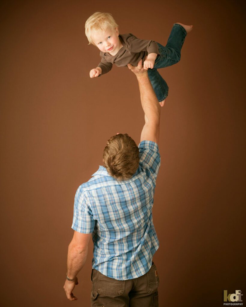 A father holds his toddler son up in the air with one hand, studio family photos, by Flagstaff photographer KDI Photography