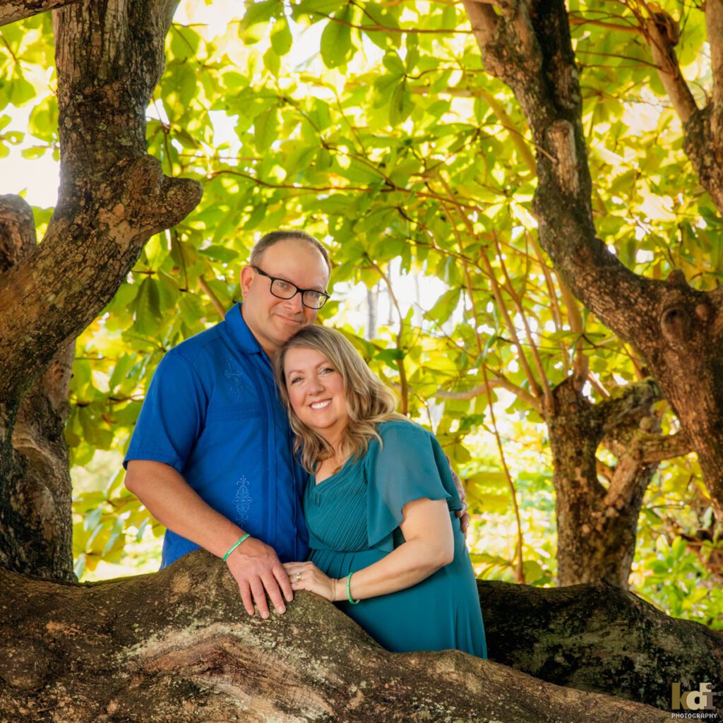 Family portrait of a husband and wife standing in the roots of a Banyan tree in Hawaii, location family photos by Flagstaff photographers KDI Photography.