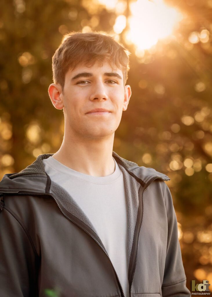 A high school hockey player in a grey hoodie sweatshirt, with the sun beaming in over his shoulder, by Flagstaff photographers, KDI Photography