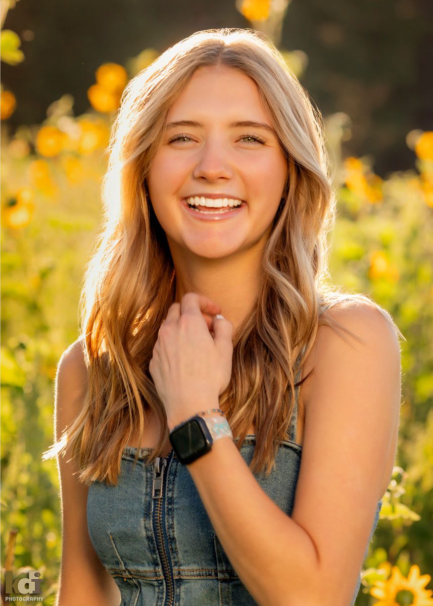 Senior photo of blonde girl in a denim dress, laughing in the wildflowers, location senior portraits by Flagstaff photographer, KDI Photography. 