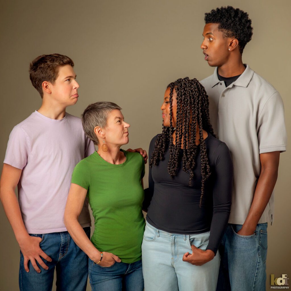 Color photograph of a studio family photo of a mother with recently shaved hair due to cancer treatment, with her teen daughter and two sons, making faces at each other, family photography by Flagstaff portrait artist KDI Photography