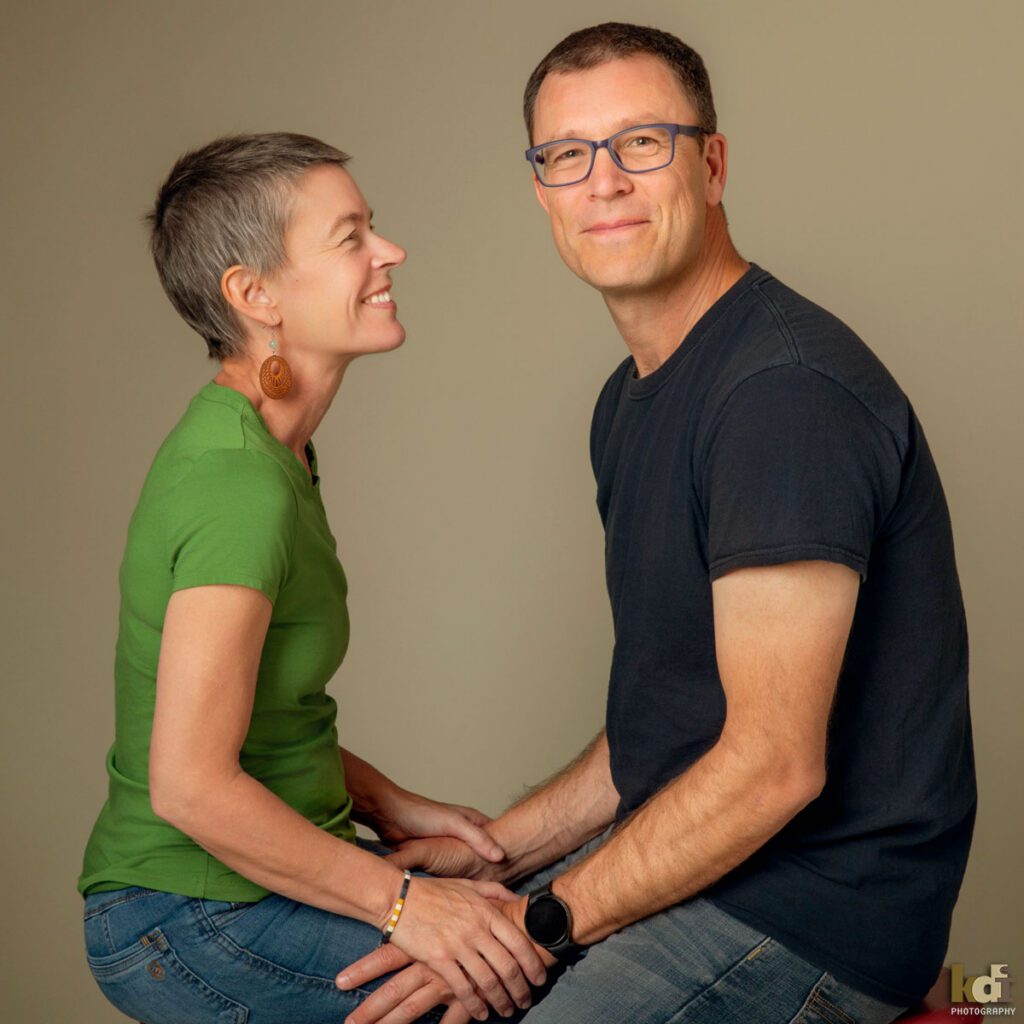 Color photograph of a studio family photo of a woman with recently shaved hair due to cancer treatment, with her husband, family photography by Flagstaff portrait artist KDI Photography