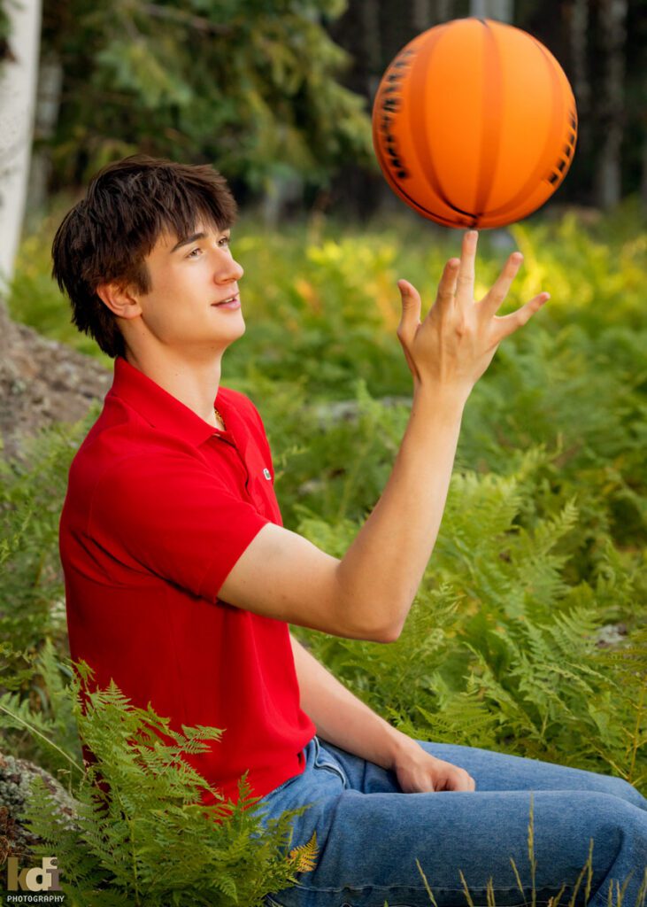 High school senior photos showing boy with brown hair, wearing red shirt, twirling basketball on his finger among the summer ferns and aspen trees, portrait photography in Flagstaff AZ by senior photographer KDI Photography