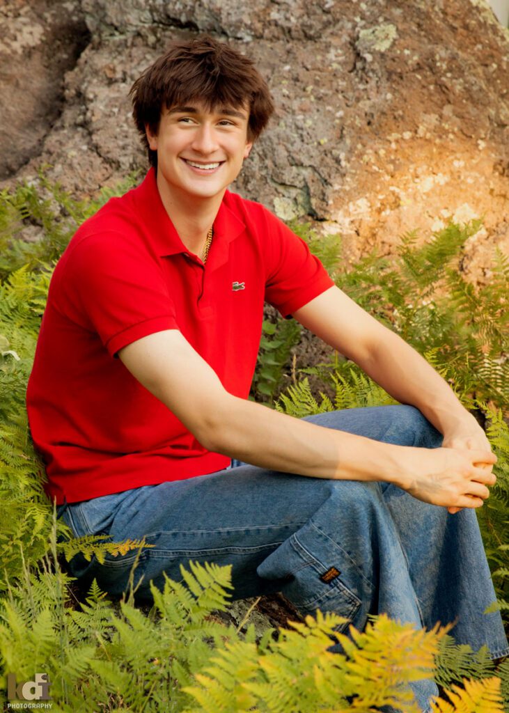 High school senior photos showing boy with brown hair, wearing red shirt, smiling off camera among the summer ferns and aspen trees, portrait photography in Flagstaff AZ by senior photographer KDI Photography