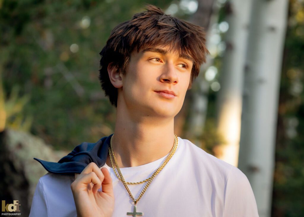 High school senior photos showing boy with brown hair, wearing white shirt, smoldering off camera among the summer ferns and aspen trees, portrait photography in Flagstaff AZ by senior photographer KDI Photography